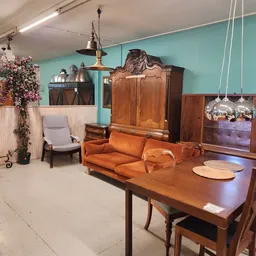 Tweedehands meubels in een kringloopwinkel: houten eettafel met stoelen, oranje bank, kasten en lampen