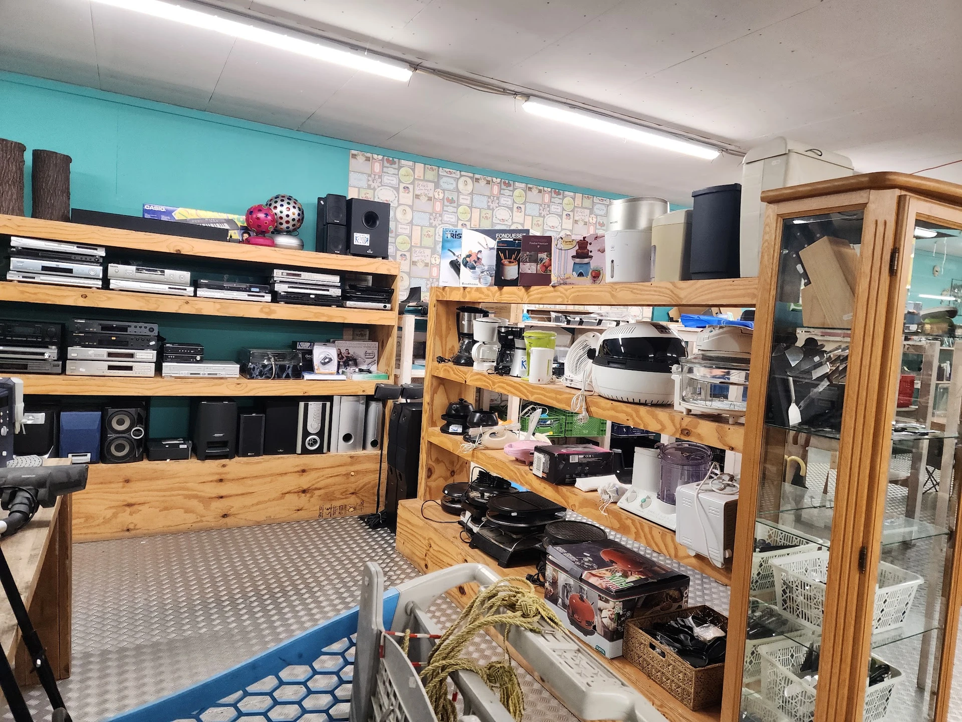 Winkelinterieur met houten stellingen vol elektronica, computers en apparaten, blauwe vloer en turquoise muur