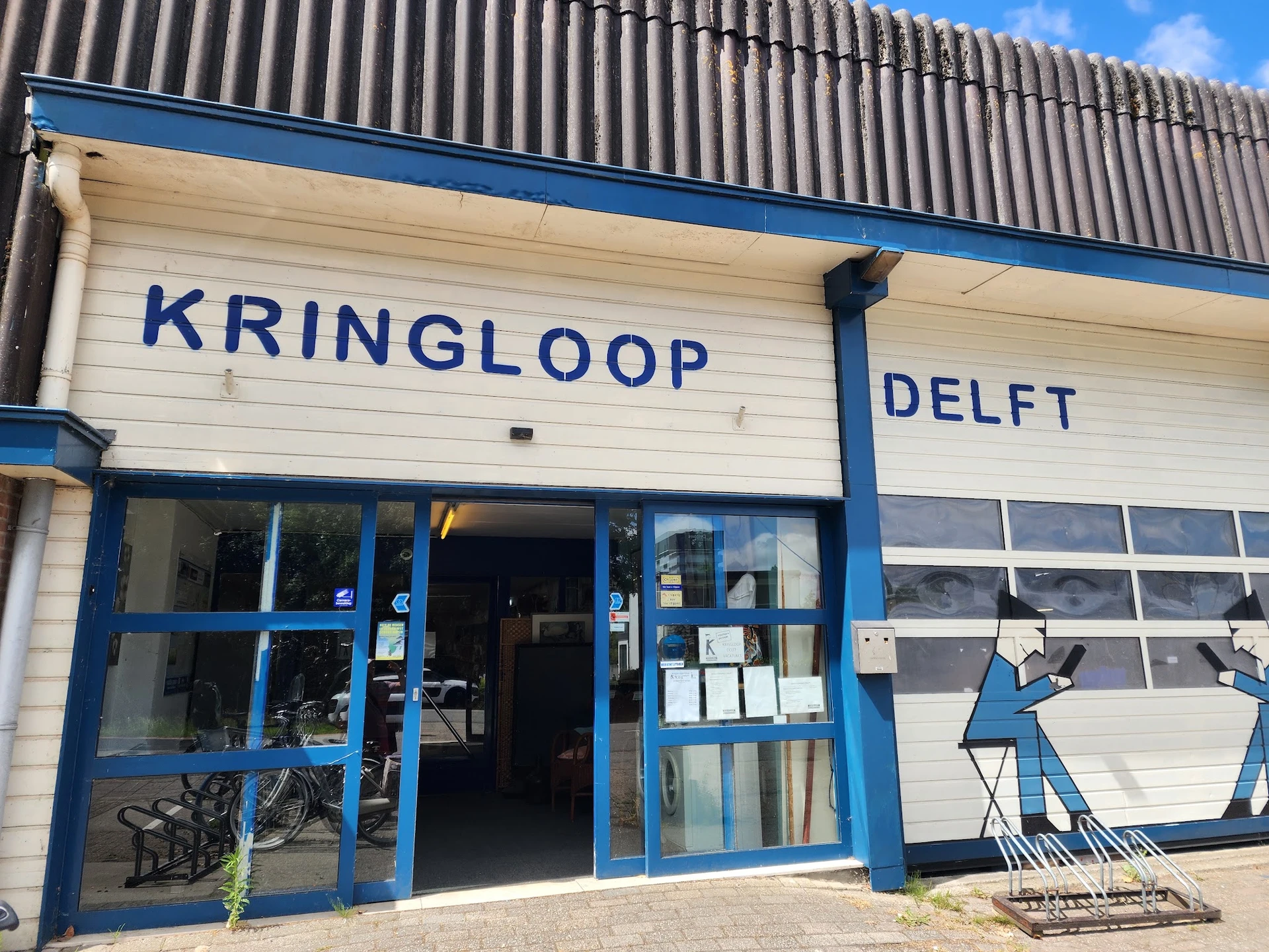 Voorgevel van kringloopwinkel met blauwe ramen en deur, naam KRINGLOOP DELFT op witte gevel