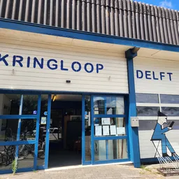 Voorgevel van kringloopwinkel met blauwe ramen en deur, naam KRINGLOOP DELFT op witte gevel