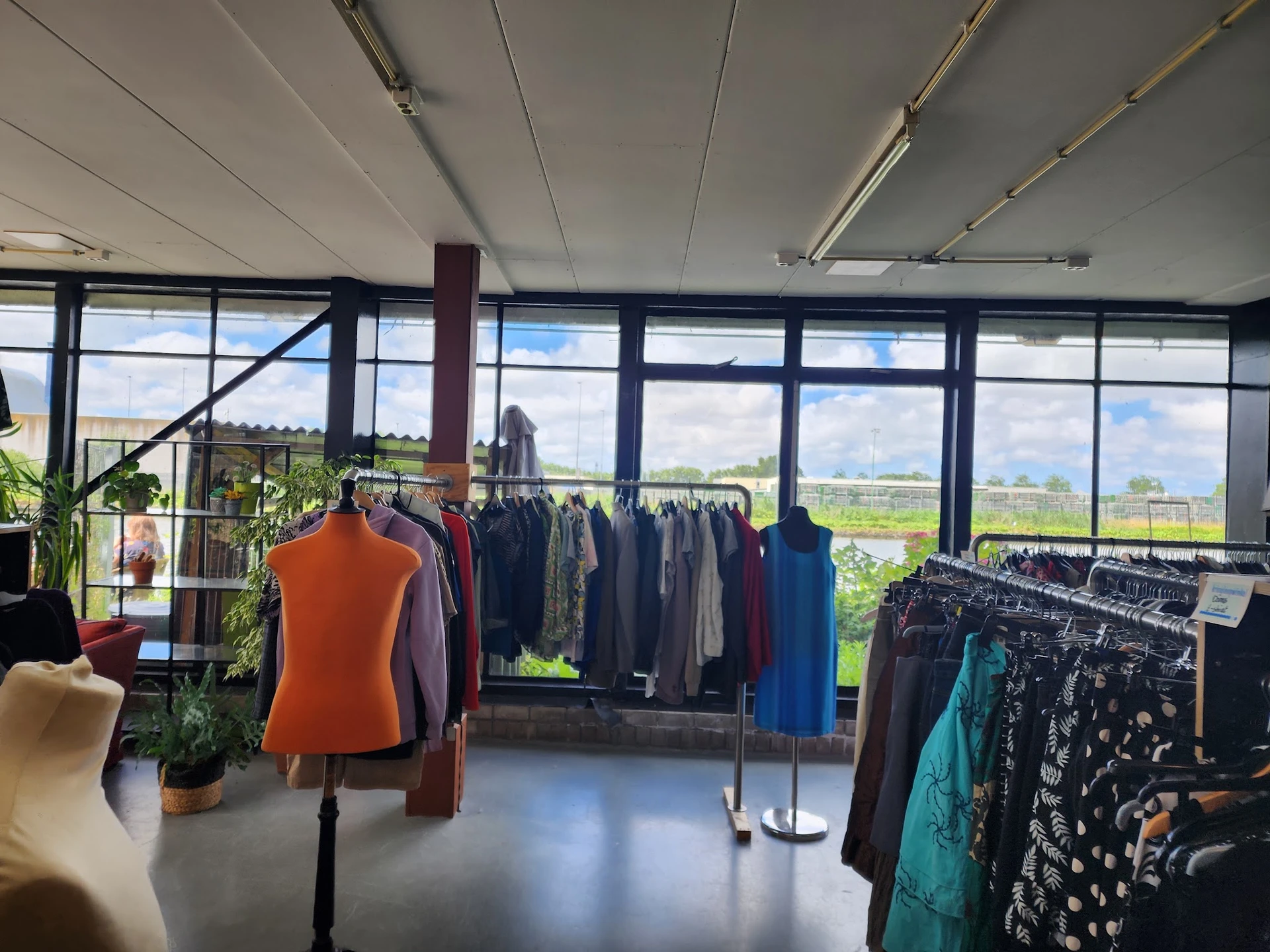 Winkelinterieur met kledingrekken en uitzicht op landschap door grote ramen