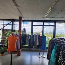 Winkelinterieur met kledingrekken en uitzicht op landschap door grote ramen