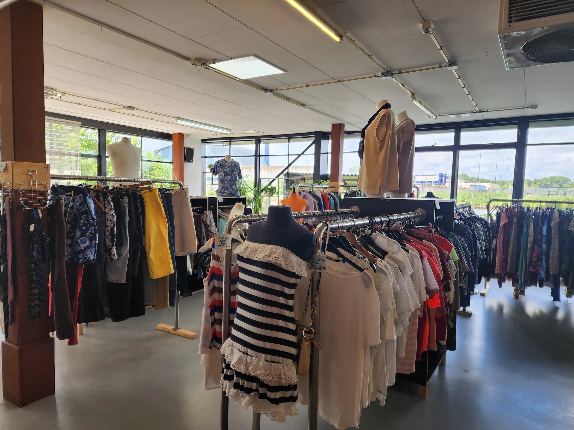 Rekken met tweedehands kleding in verschillende kleuren en stijlen in een lichtrrijke winkelruimte