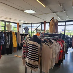 Rekken met tweedehands kleding in verschillende kleuren en stijlen in een lichtrrijke winkelruimte
