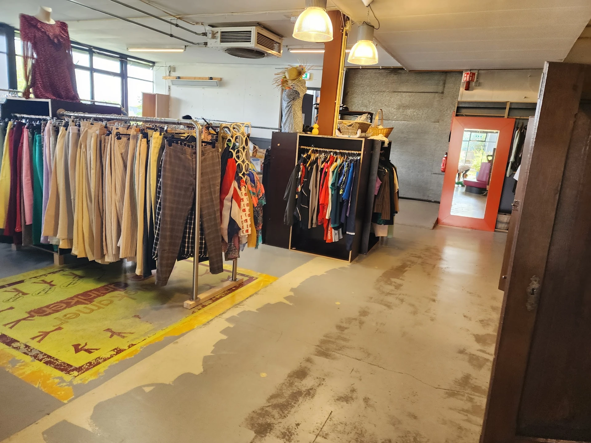 Winkelvloer met kledingrekken en uitgestalde tweedehands kleding, gele vloermarkering en rode deur op achtergrond