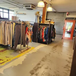 Winkelvloer met kledingrekken en uitgestalde tweedehands kleding, gele vloermarkering en rode deur op achtergrond