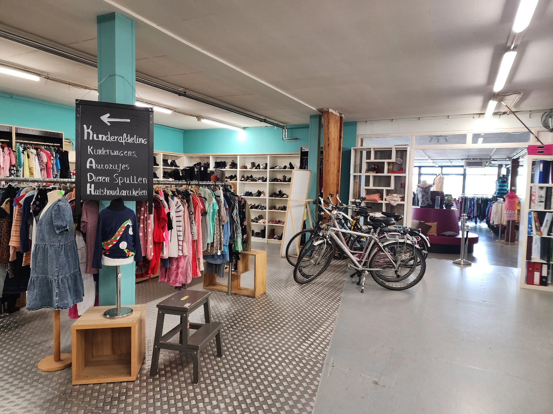 Winkelvloer met kledingrekken, fietsen, schoenenrek en houten meubels in een kringloopwinkel