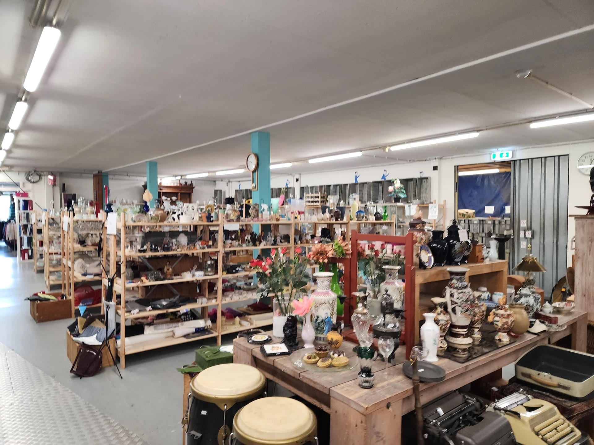 Ruim magazijnachtig interieur met houten stellingen vol huishoudartikelen, servies en decoratievoorwerpen