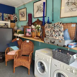 Afdeling met wasmachines, rieten stoelen, kunstwerk en decoratieve items op turquoise muur