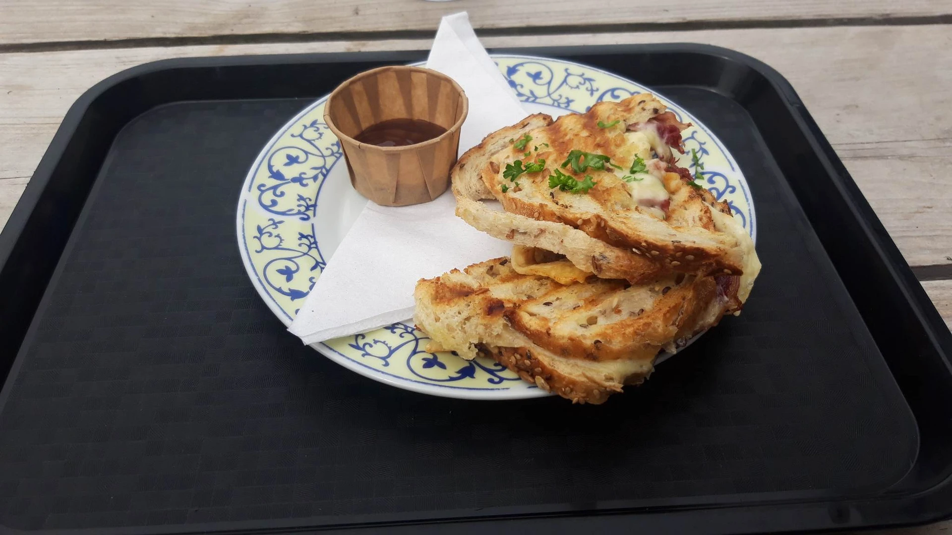 Bord met twee Franse toast sneetjes, garnished met groene kruiden, en een kopje saus op een decoratief bord met blauwe rand