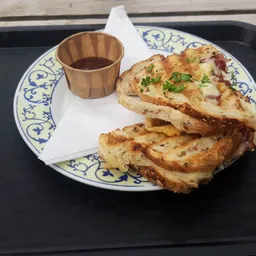 Bord met twee Franse toast sneetjes, garnished met groene kruiden, en een kopje saus op een decoratief bord met blauwe rand