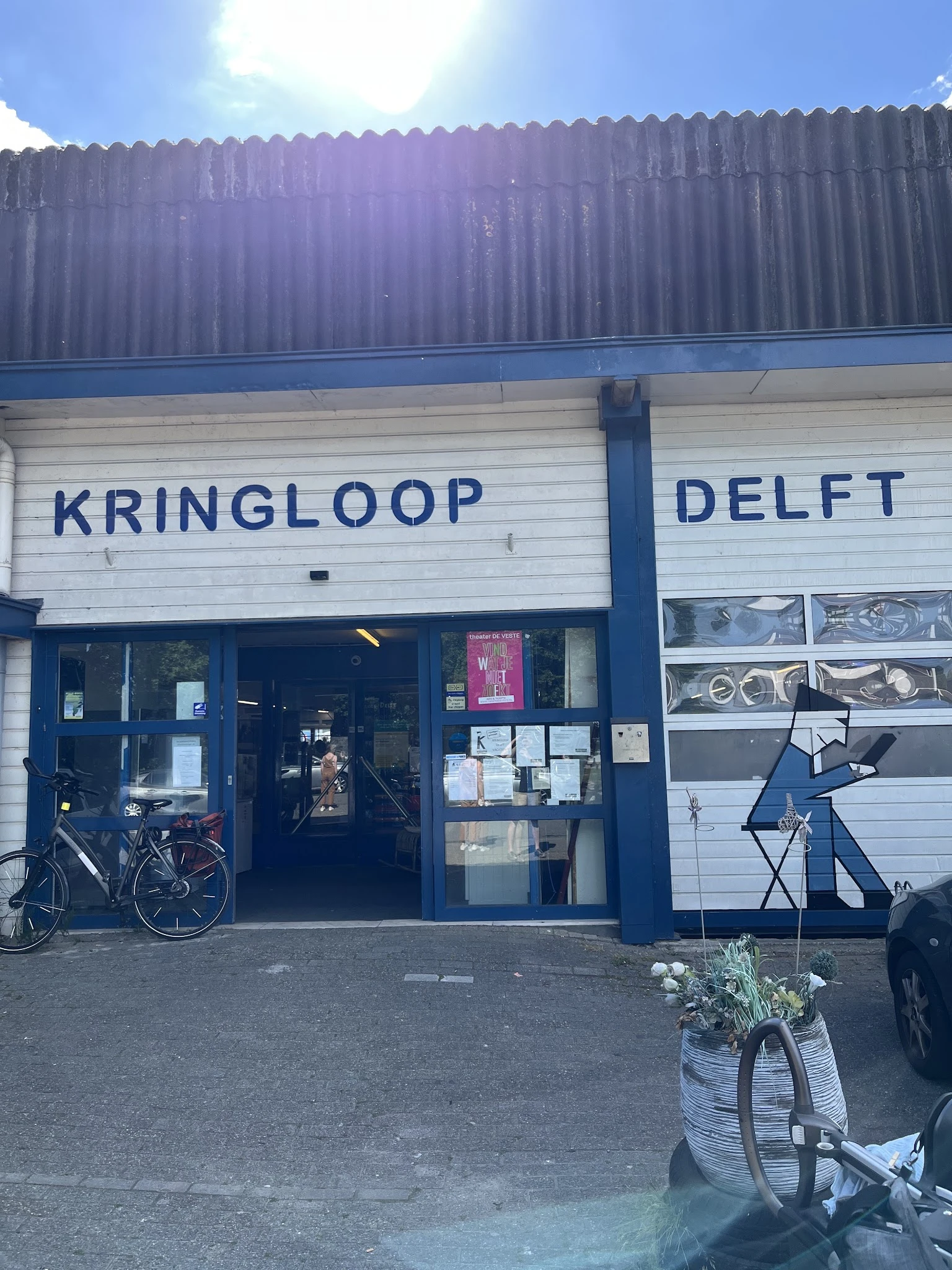 Voorgevel van kringloopwinkel met blauwe ramen en deur, winkelnaam leesbaar, fiets tegen gevel