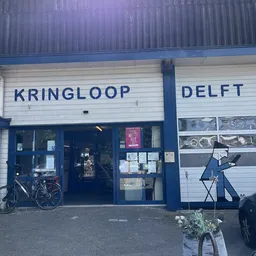 Voorgevel van kringloopwinkel met blauwe ramen en deur, winkelnaam leesbaar, fiets tegen gevel