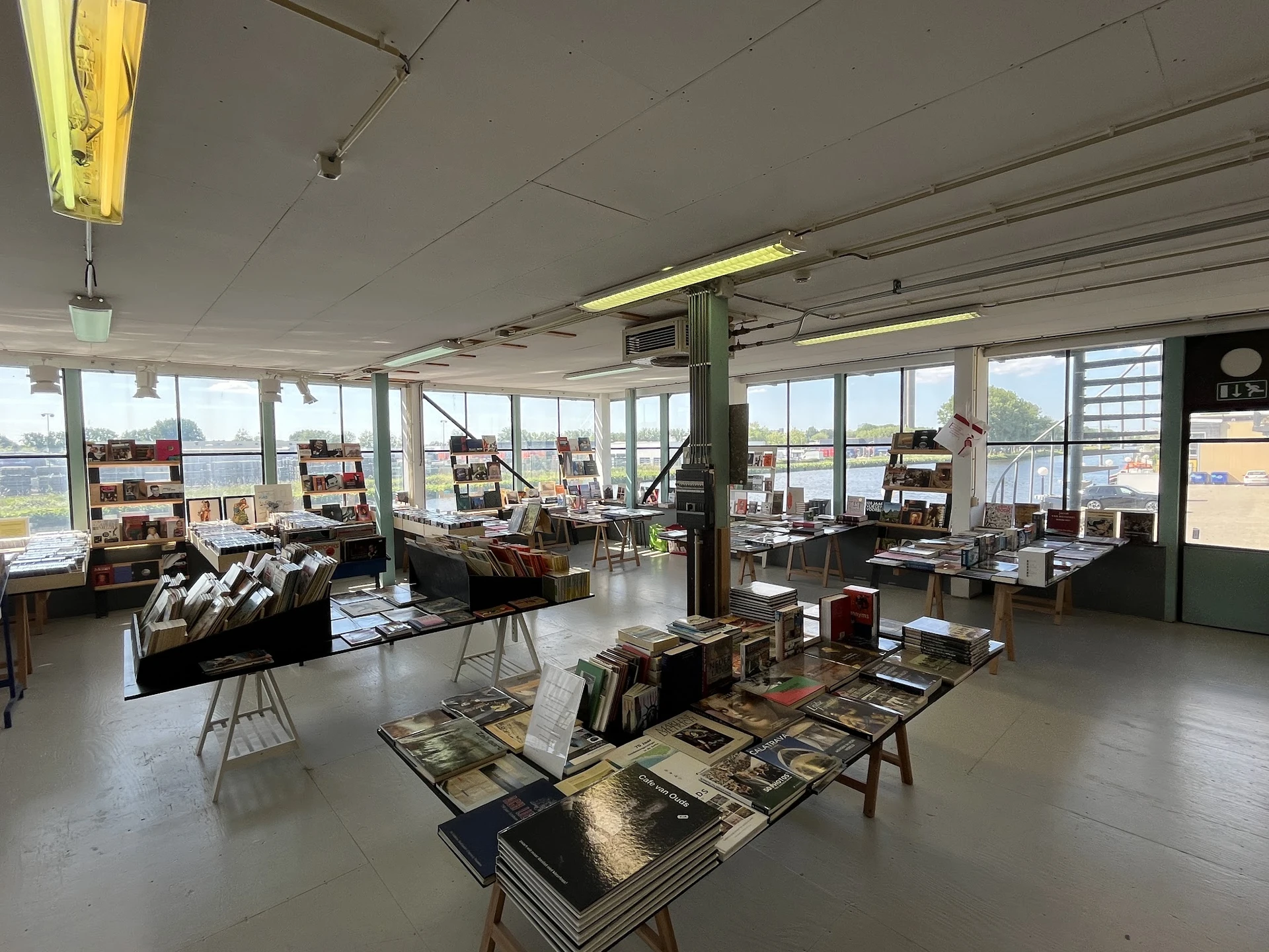 Ruim interieur van kringloopwinkel met diverse tweedehands artikelen op tafels en stellingen, grote ramen met uitzicht