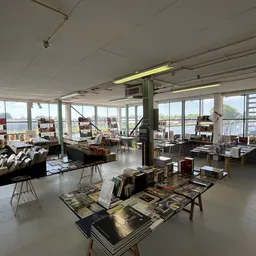 Ruim interieur van kringloopwinkel met diverse tweedehands artikelen op tafels en stellingen, grote ramen met uitzicht