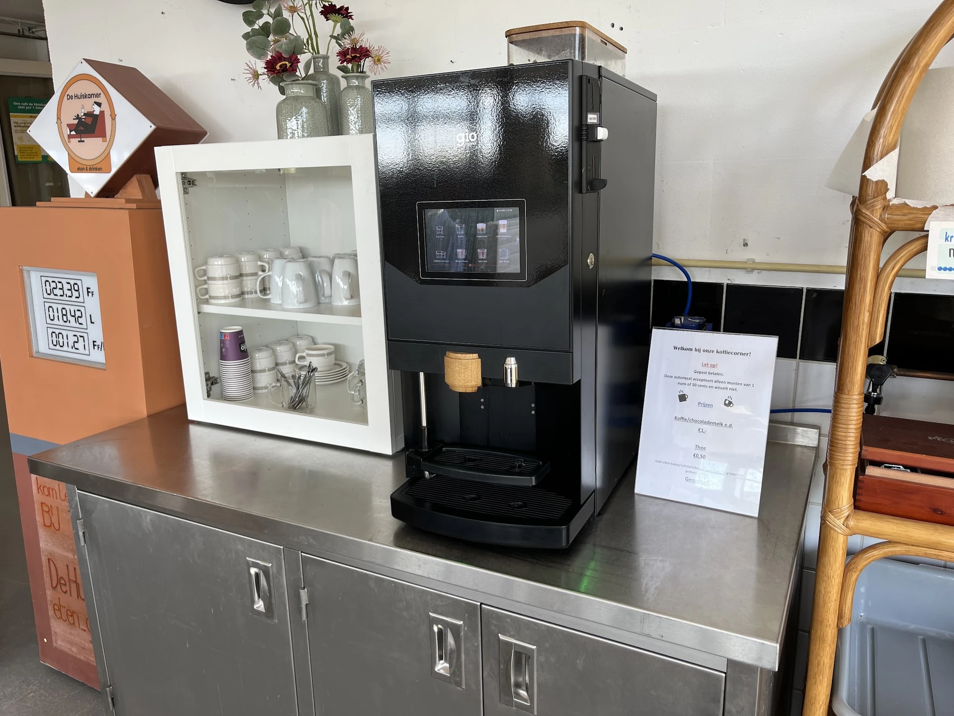 Zwarte koffieautomaat met displayscherm op een grijze werktafel, omgeven door andere winkelinventaris