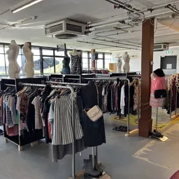Rekken met tweedehands kleding, waaronder jurken, broeken en jassen, met etalagepoppen in een ruim kringloopwinkelbinnenruimt