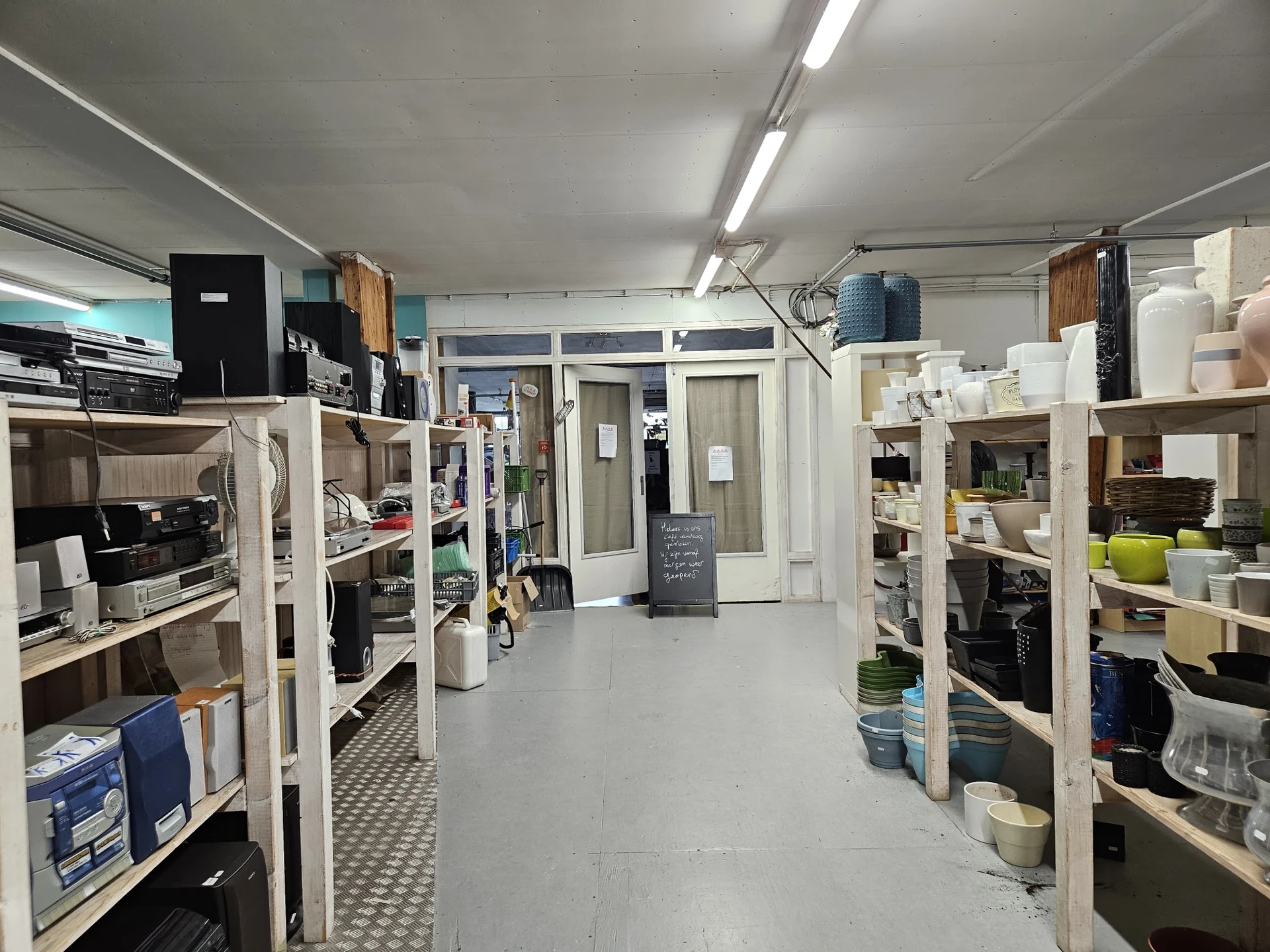 Winkelvloer van kringloopwinkel met witte stellingen vol met huishoudartikelen en dozen aan beide zijden