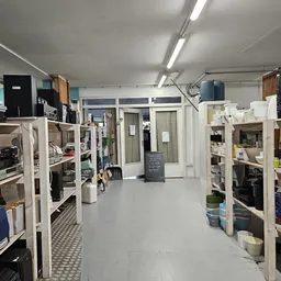 Winkelvloer van kringloopwinkel met witte stellingen vol met huishoudartikelen en dozen aan beide zijden