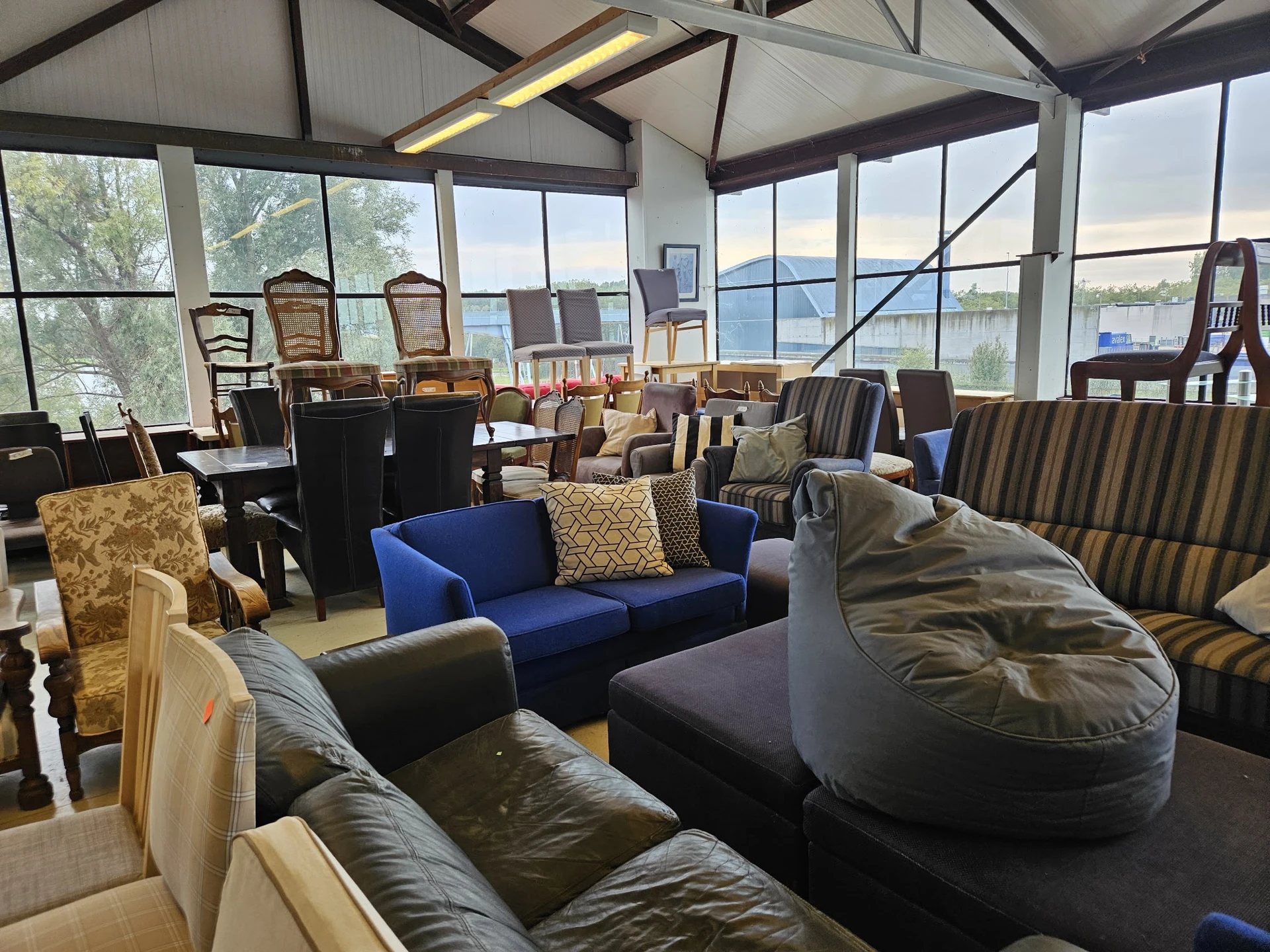 Ruime winkelhal met diverse meubels: blauwe bank, lederen fauteuils, bean bags en stoelen, grote ramen met uitzicht