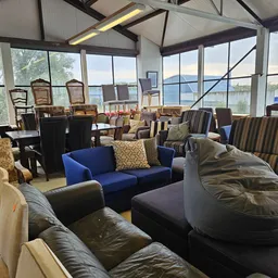 Ruime winkelhal met diverse meubels: blauwe bank, lederen fauteuils, bean bags en stoelen, grote ramen met uitzicht