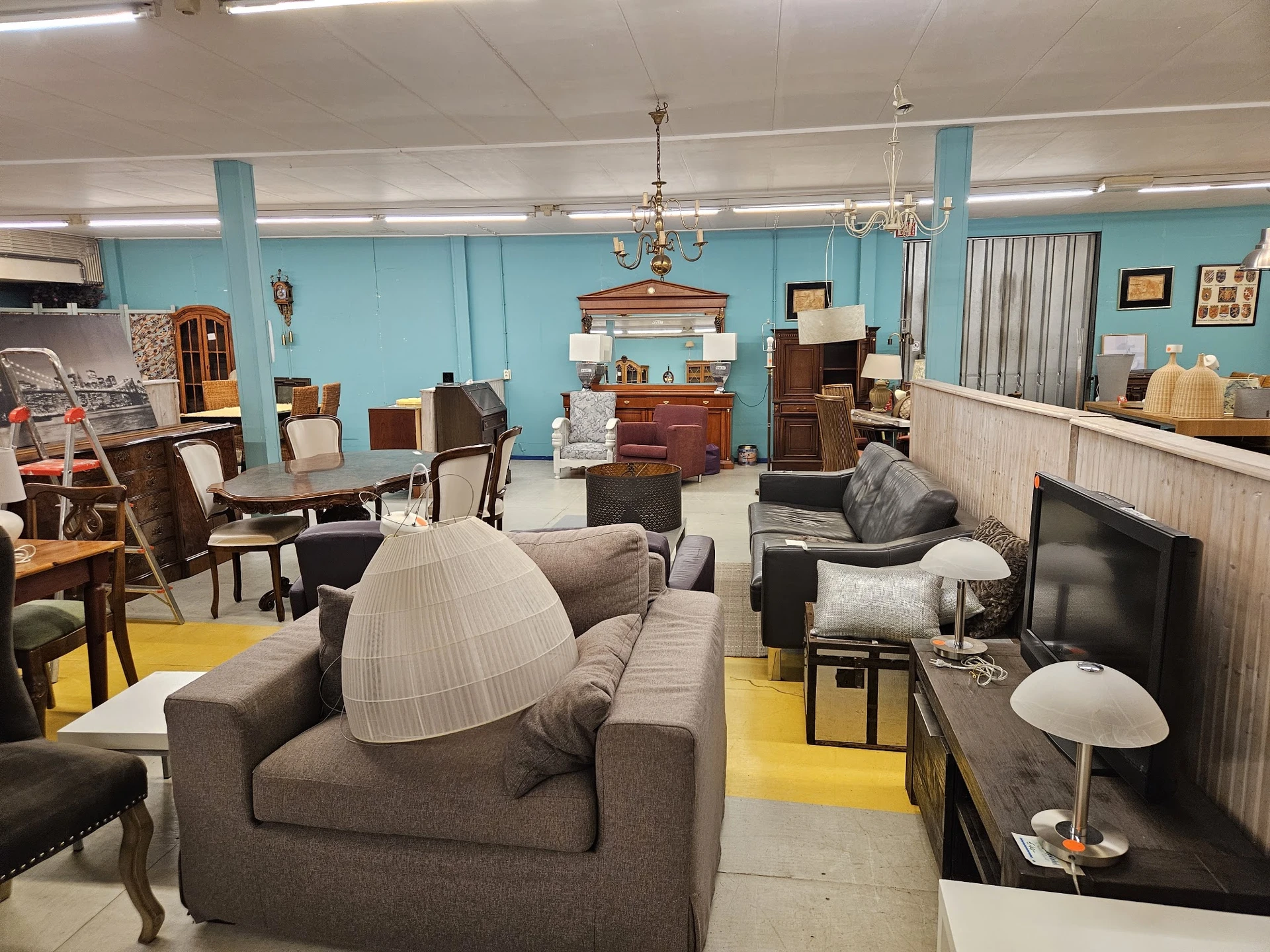 Winkelvloer met tweedehands meubels: fauteuils, banken, kasten en lampen onder turquoise wanden