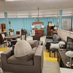 Winkelvloer met tweedehands meubels: fauteuils, banken, kasten en lampen onder turquoise wanden