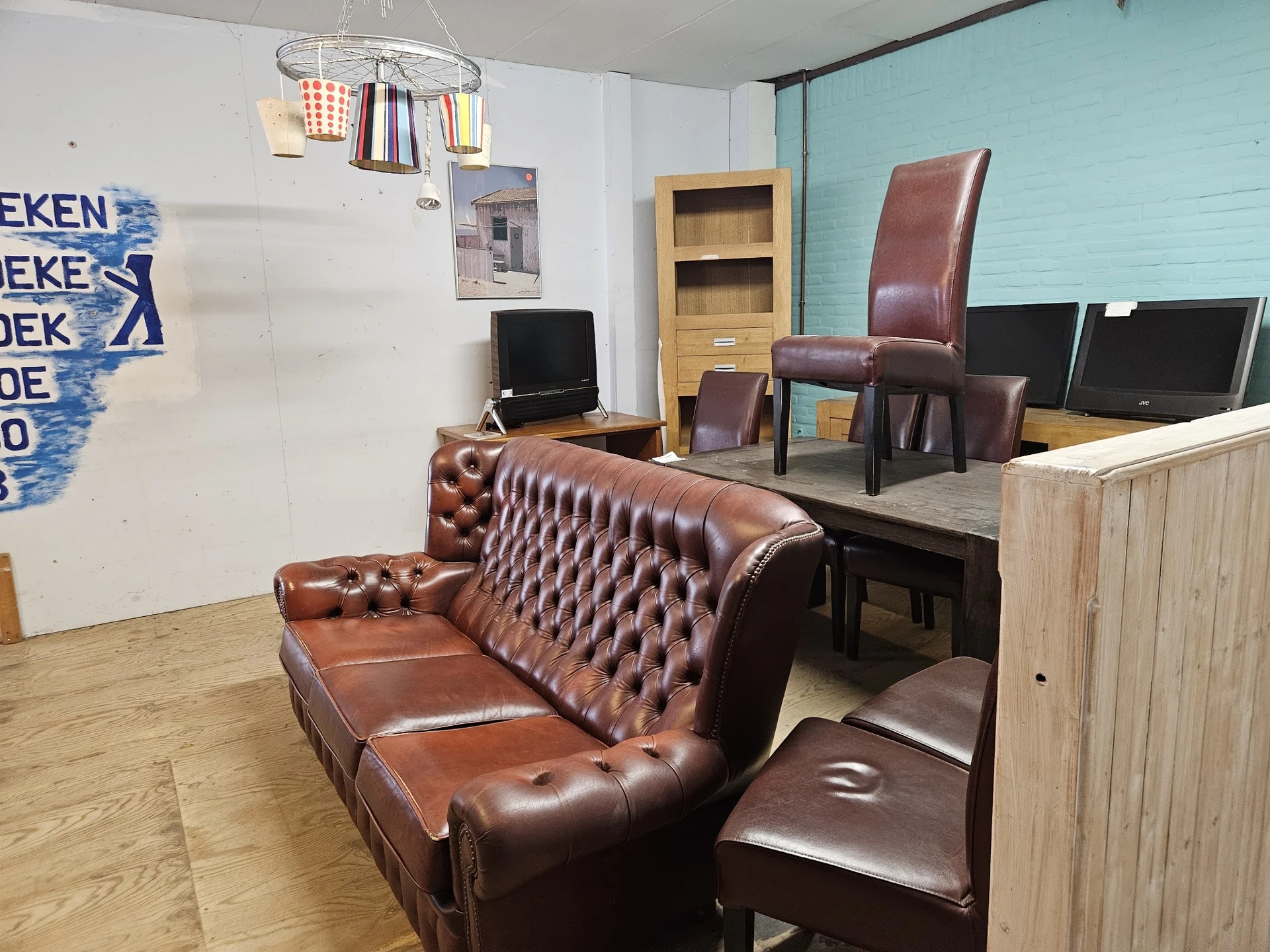 Winkelvloer met bruinleren Chesterfield-bank, houten toonbank, monitoren en diverse meubels in een kringloopwinkel