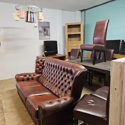 Winkelvloer met bruinleren Chesterfield-bank, houten toonbank, monitoren en diverse meubels in een kringloopwinkel