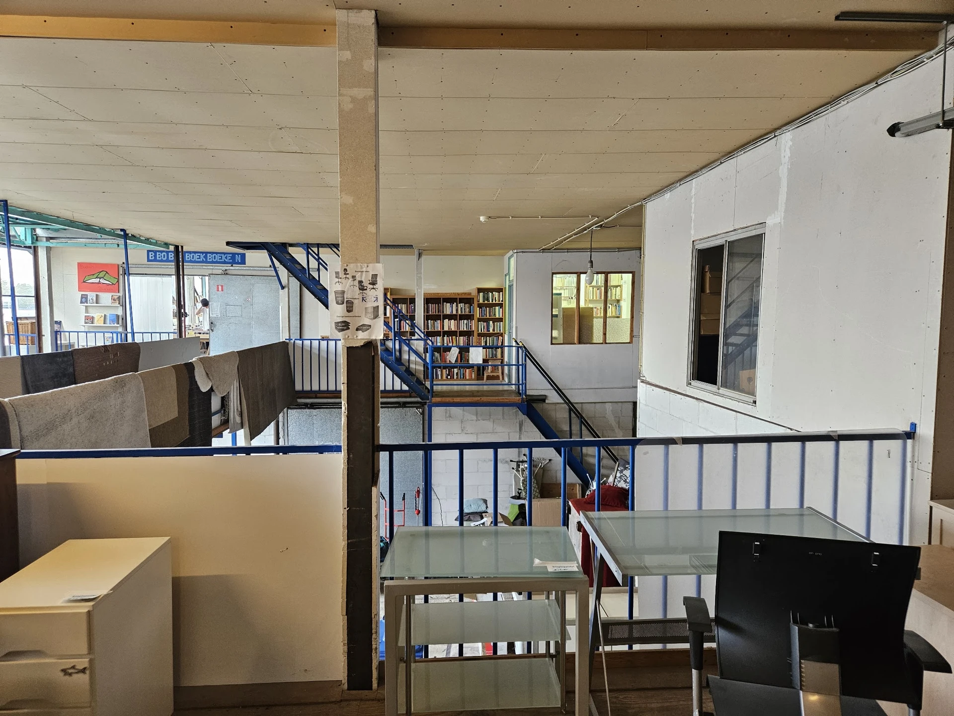 Bovenaanzicht van de winkelvloer met trappen, leuningen, boekenkasten en verschillende afdelingen in een tweelaagse kringloop