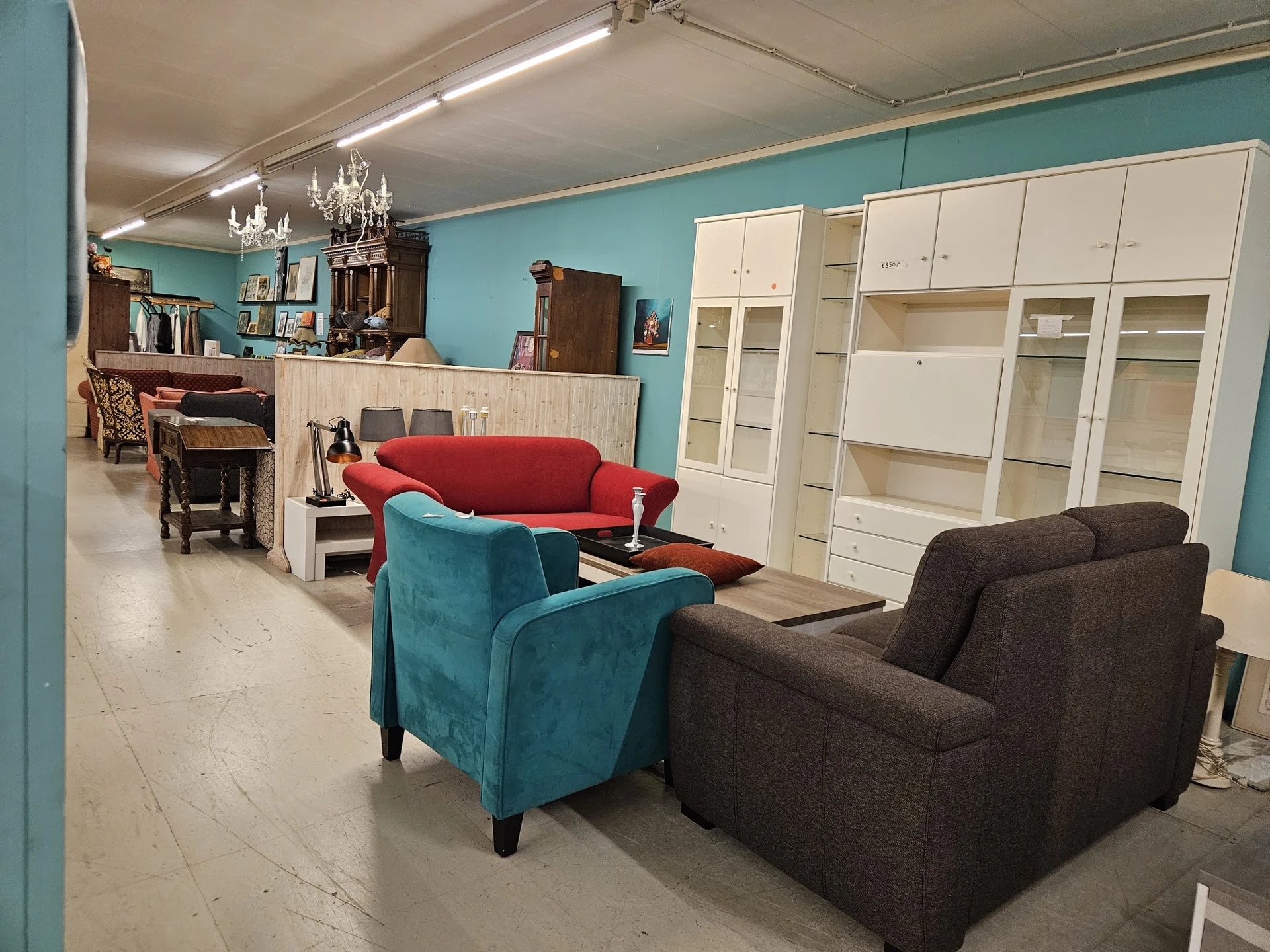 Winkelinterieur met diverse zitmeubelen: rode en turquoise fauteuils, donkerbruine stoelen en witte kastenwand met glazen deu