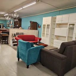 Winkelinterieur met diverse zitmeubelen: rode en turquoise fauteuils, donkerbruine stoelen en witte kastenwand met glazen deu