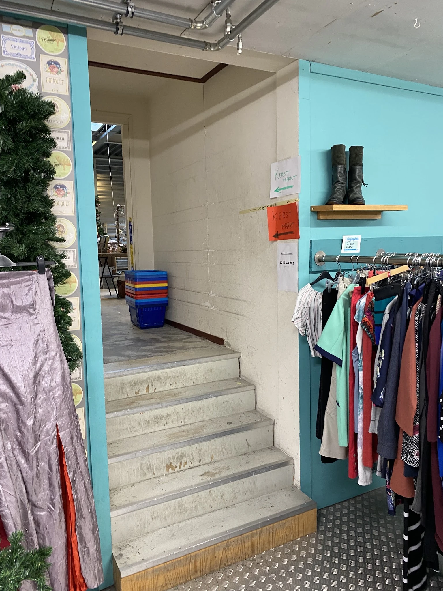Trapopgang naar winkelruimte met rekken vol tweedehands kleding, schoenen op plank en kleurrijke kratten