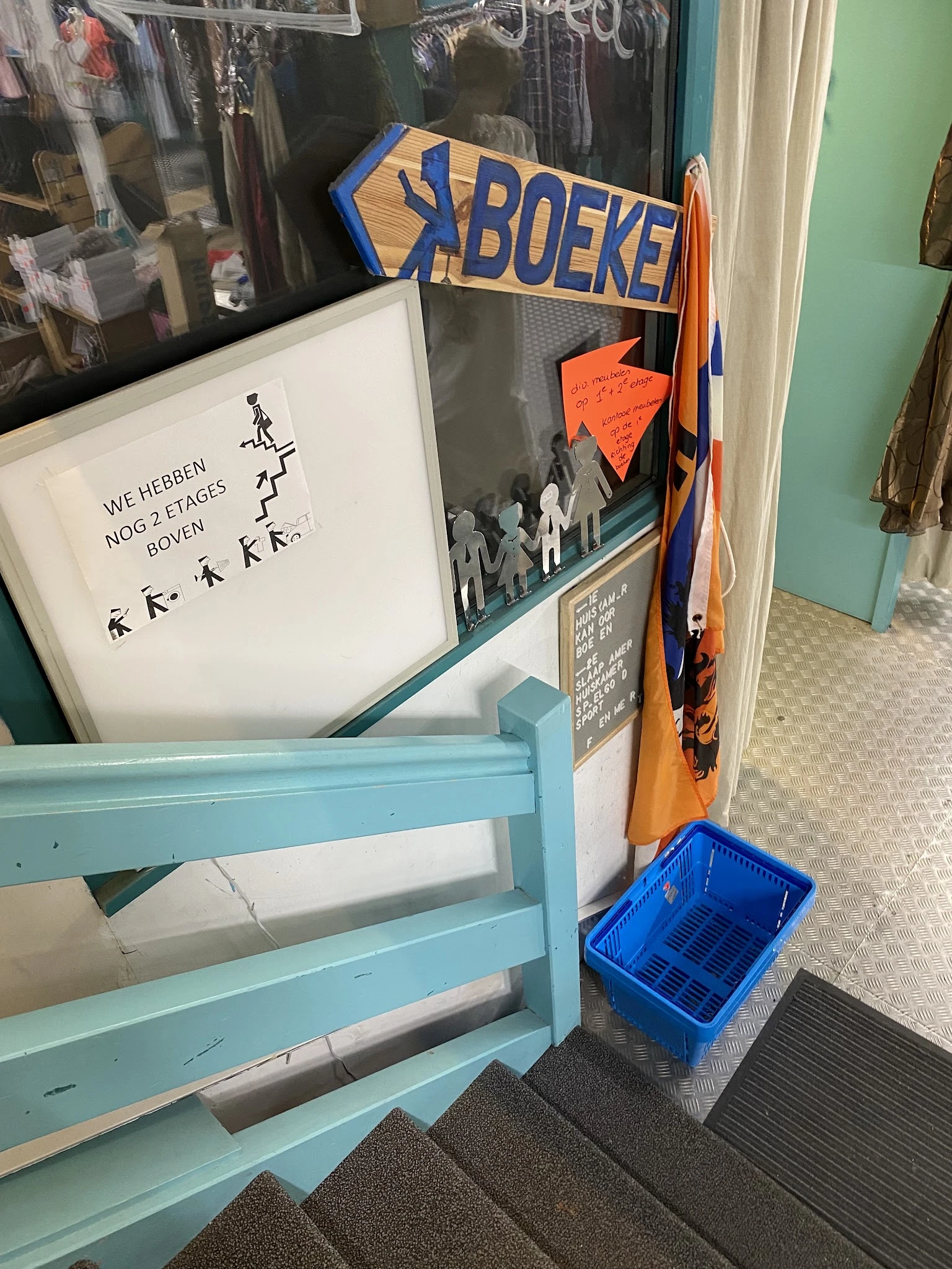 Winkelhoek met blauwe stellage, witte bord met Nederlands handschrift, oranje bord en blauwe krat op vloer