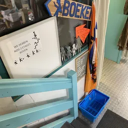 Winkelhoek met blauwe stellage, witte bord met Nederlands handschrift, oranje bord en blauwe krat op vloer