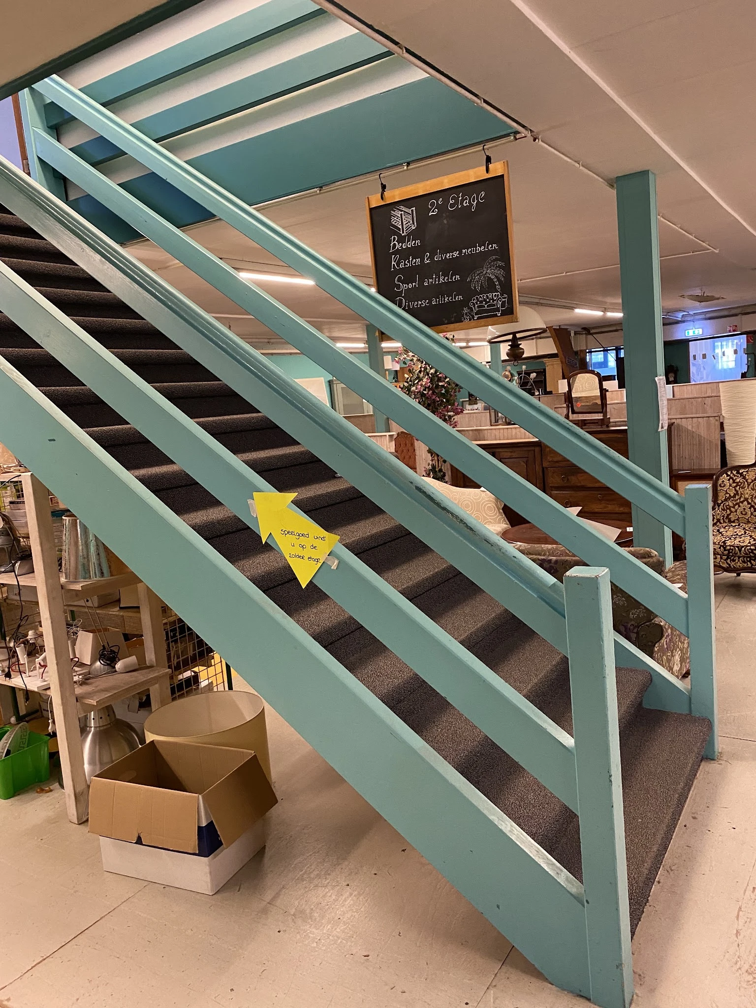 Trap met turquoise leuning en gele waarschuwingssticker in kringloopwinkel