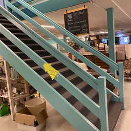 Trap met turquoise leuning en gele waarschuwingssticker in kringloopwinkel