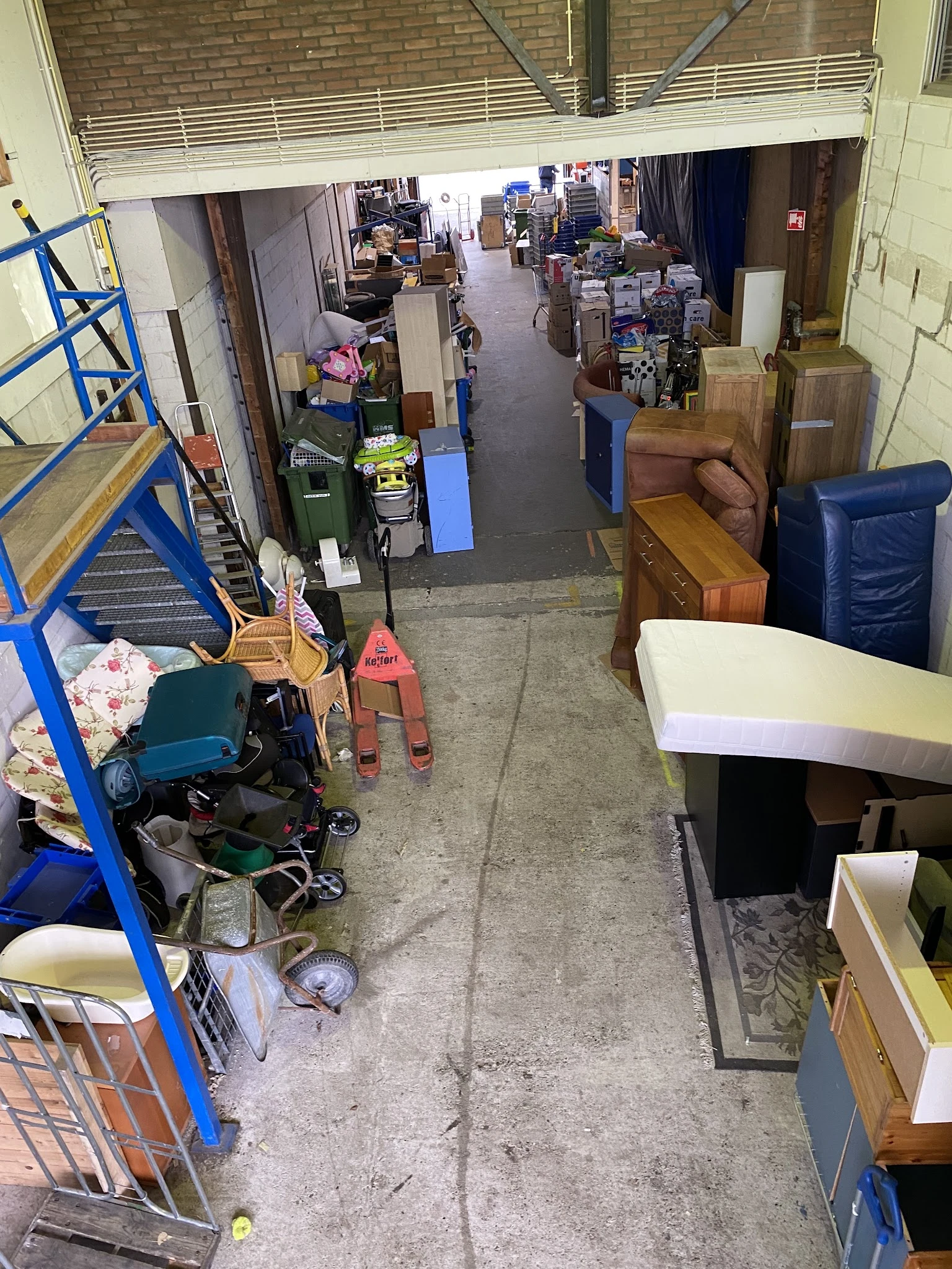Overzicht van winkelvloer met uiteenlopende spullen, meubilair en dozen in een kringloopwinkel