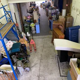 Overzicht van winkelvloer met uiteenlopende spullen, meubilair en dozen in een kringloopwinkel