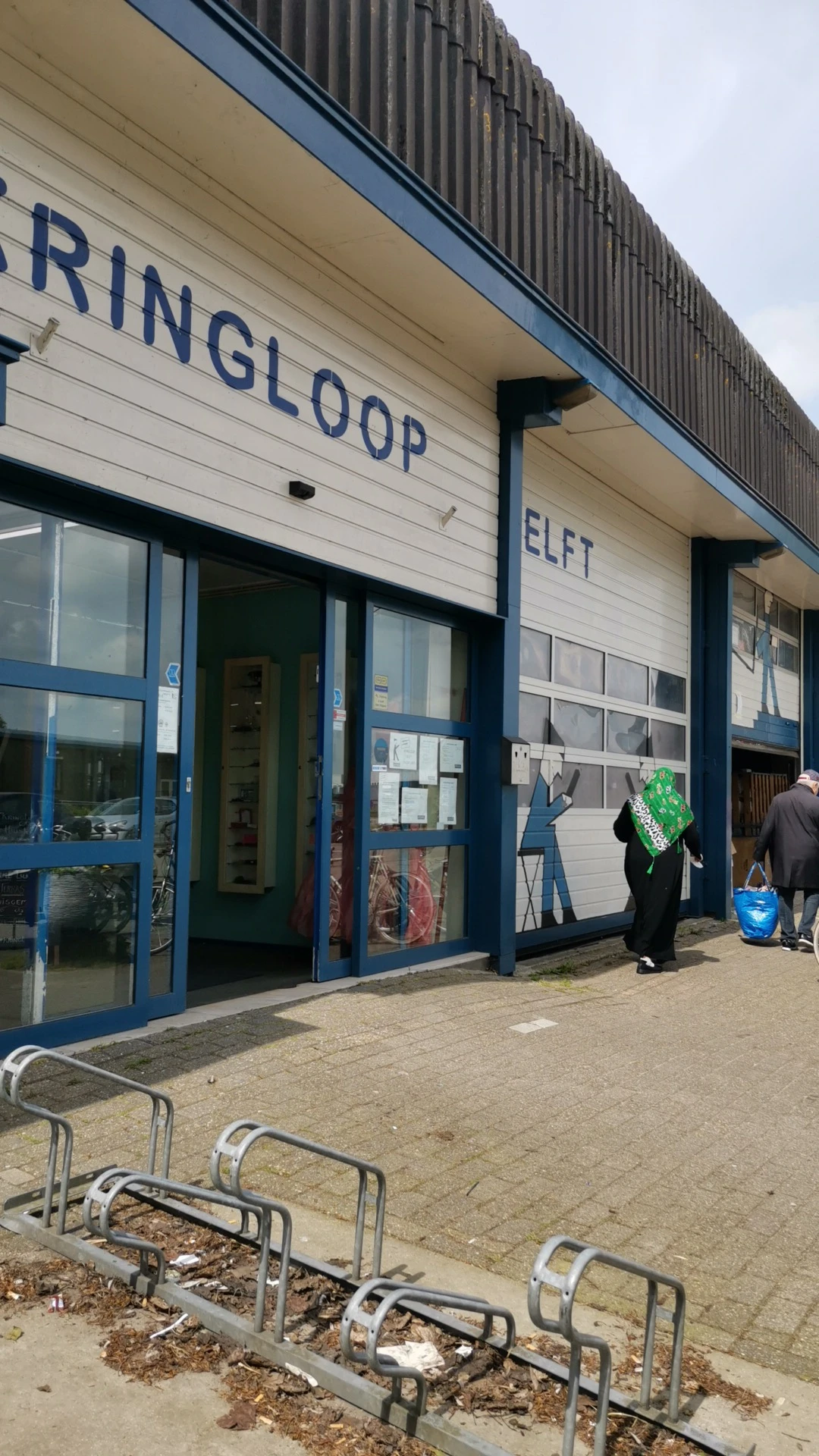 Winkelvoorgevel met blauwe ramen en deuren, witte bovenomlijsting met letters, mannequin in etalage