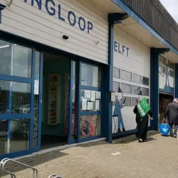 Winkelvoorgevel met blauwe ramen en deuren, witte bovenomlijsting met letters, mannequin in etalage