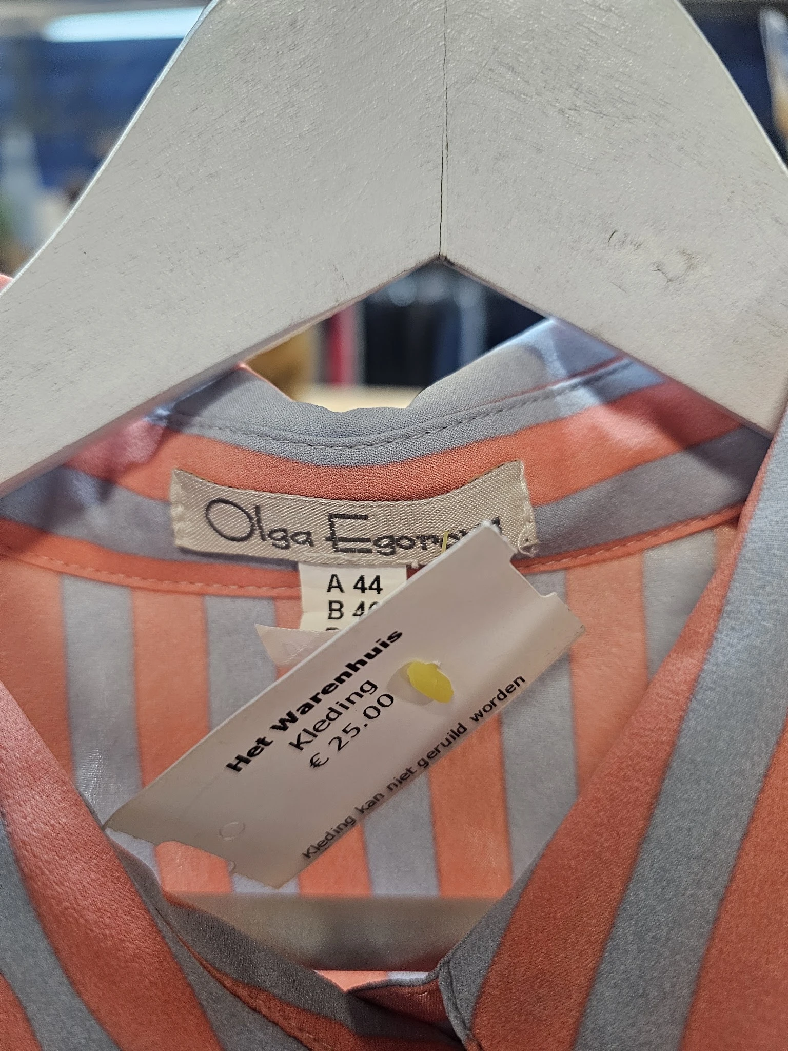 Close-up van een oranje-grijs gestreept kledingstuk met label 'Olga Egorna' en maat A 44, B 46, waarschijndig een vintage ite