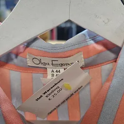 Close-up van een oranje-grijs gestreept kledingstuk met label 'Olga Egorna' en maat A 44, B 46, waarschijndig een vintage ite