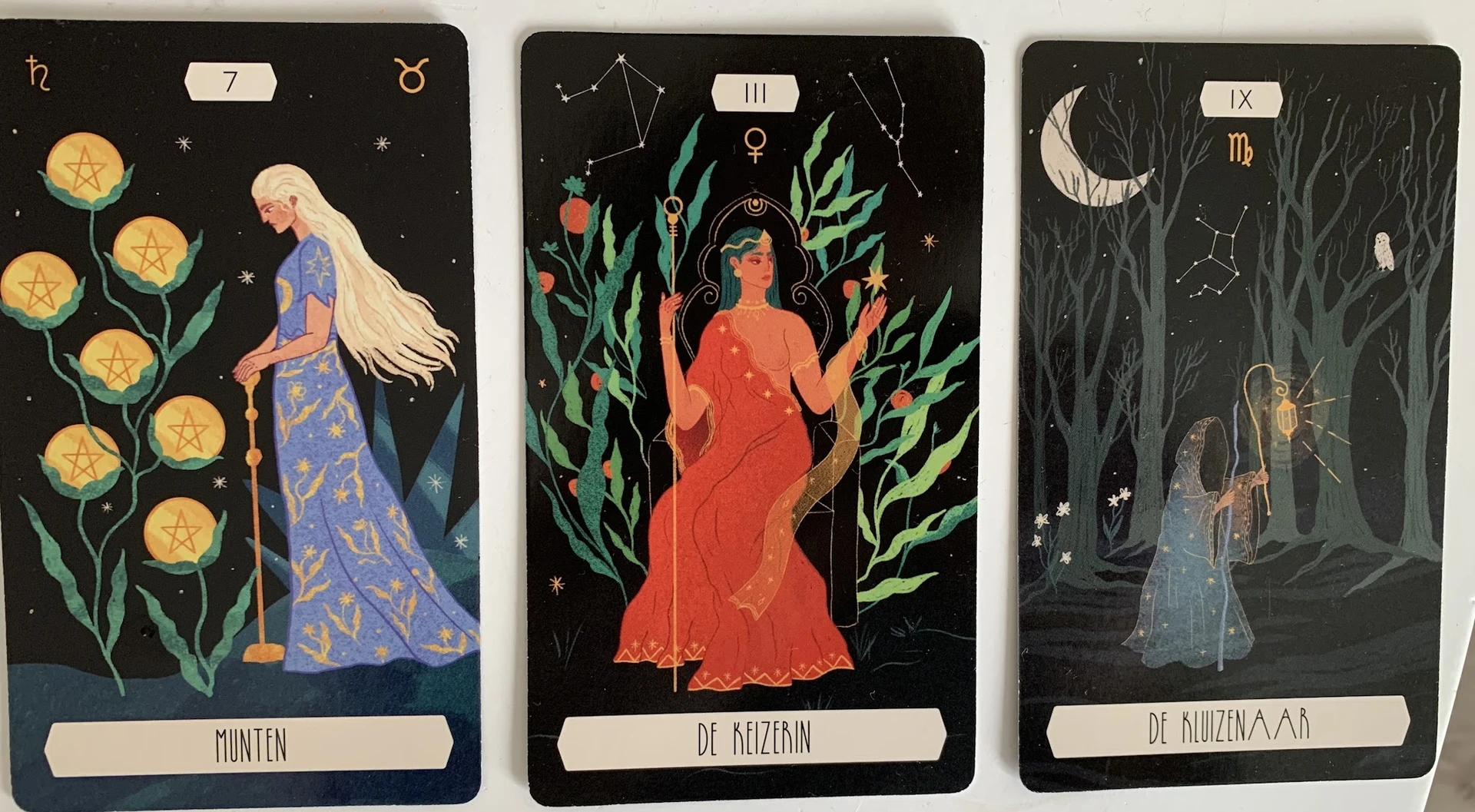 Drie tarotkaarten met illustraties van vrouwenfiguren en astrologische symbolen op zwarte achtergrond