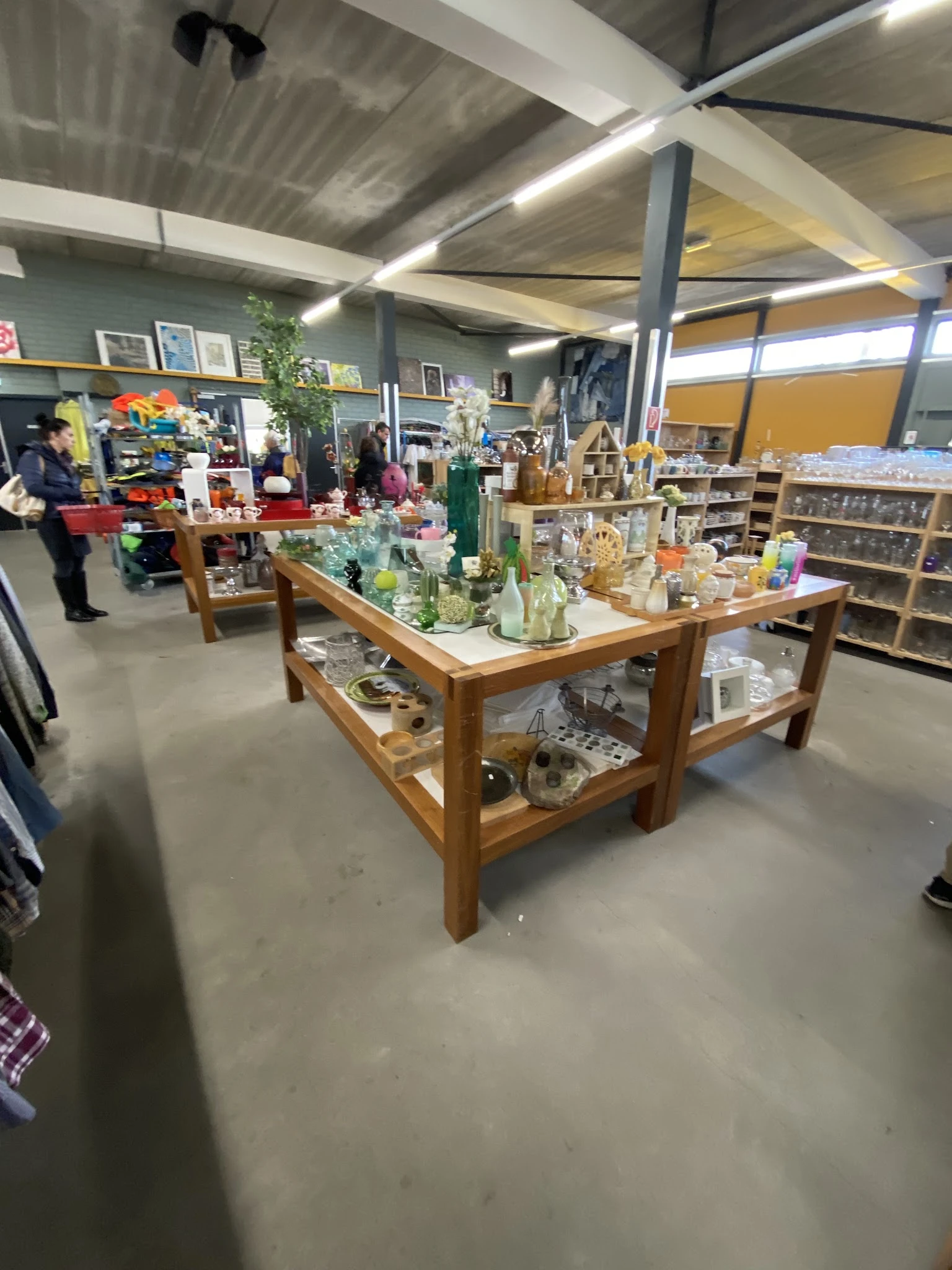 Winkelvloer met houten display tafels vol met huishoudspullen, vazen en decoratieartikelen in een kringloopwinkel