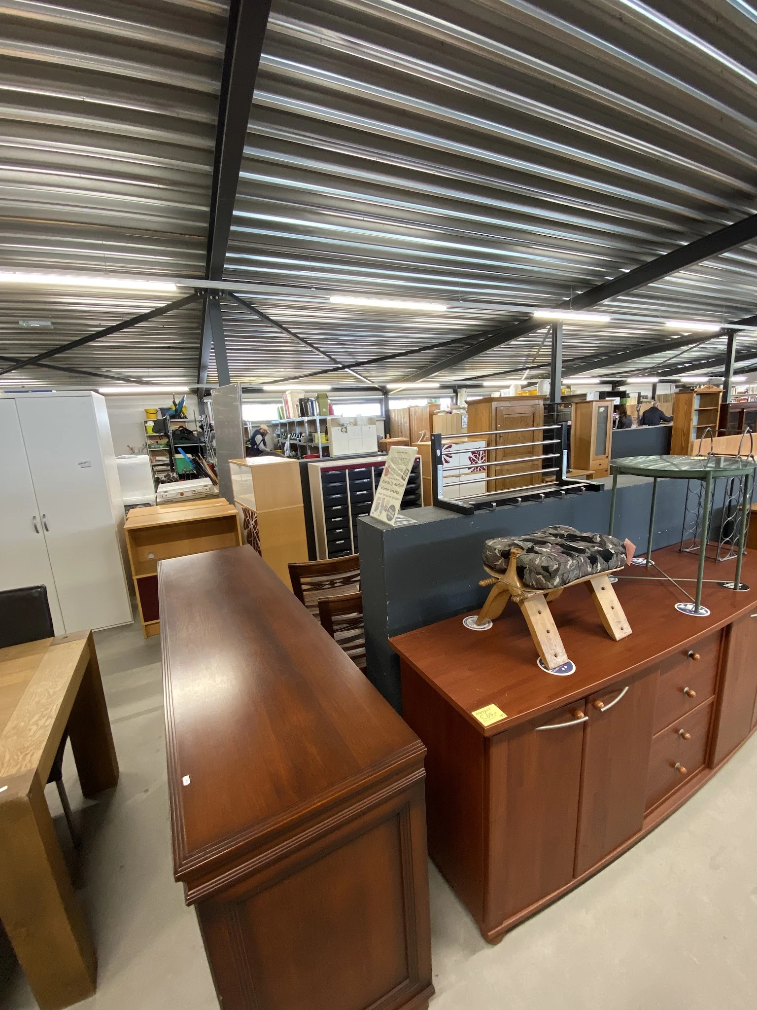 Winkelvloer met uiteenlopende meubels: kasten, laden, tafels en stoelen uitgestald onder industriële verlichting