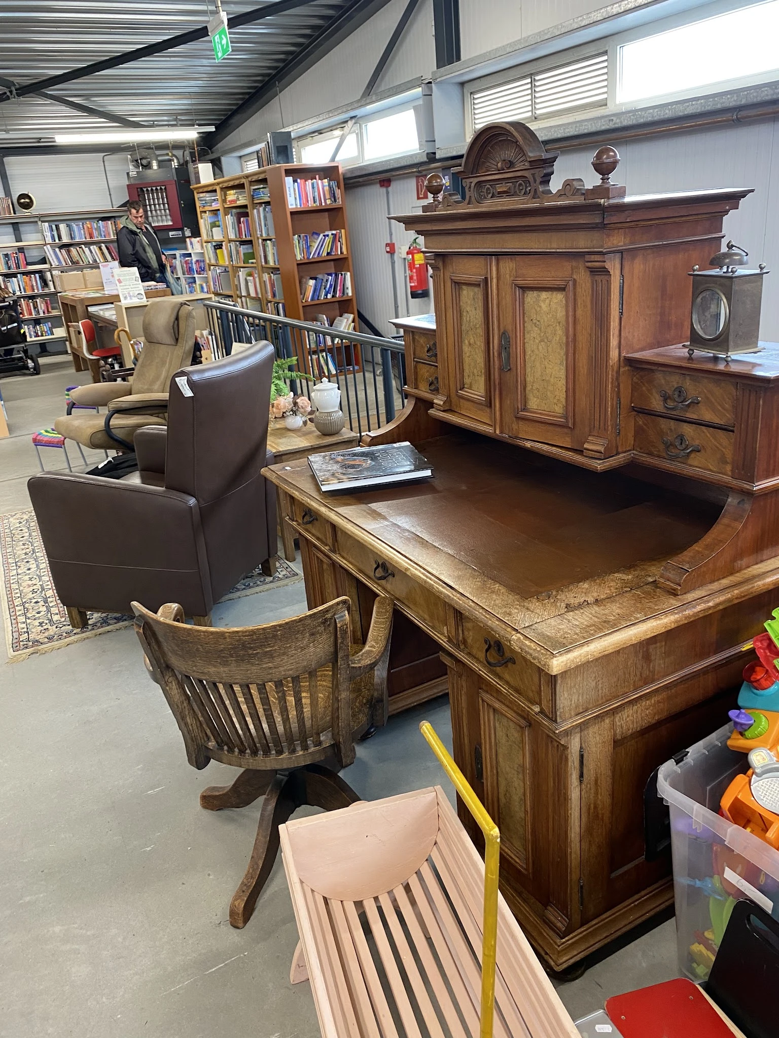 Houten bureau en stoelen in een kringloopwinkel met boekenrekken en ander meubilair op de achtergrond