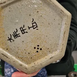 Close-up van een beige aardewerken schaaltje met Aziatische karakters en decoratieve stippen, gehouden in een hand