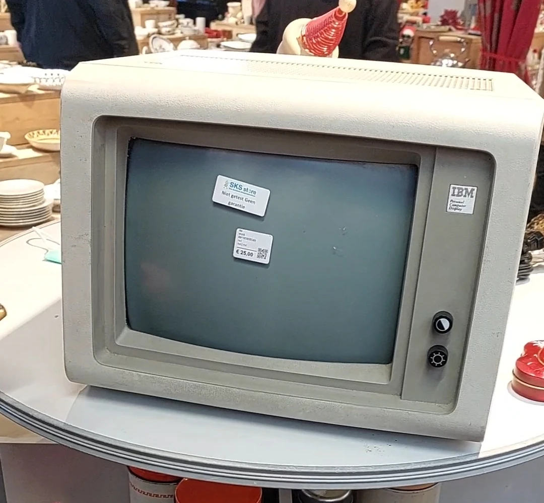 Vintage IBM-computer met grijs scherm op witte tafel, met stickers op het beeldscherm