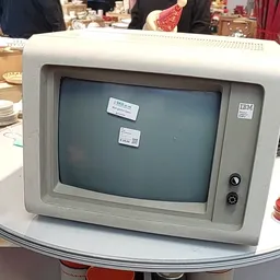 Vintage IBM-computer met grijs scherm op witte tafel, met stickers op het beeldscherm